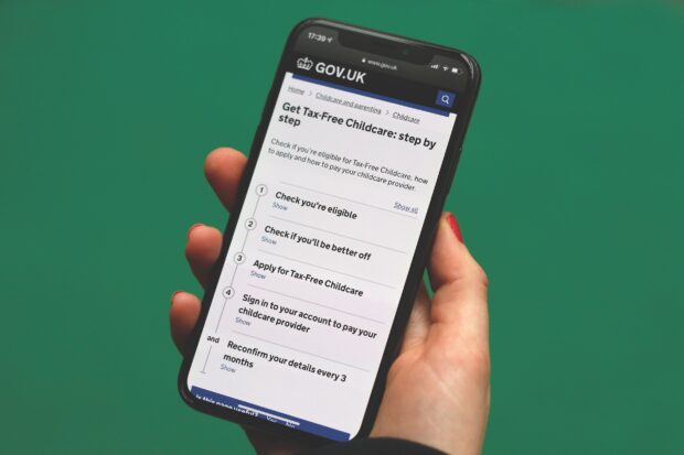 Someone holding a smartphone showing a step by step overviewing of getting tax-free childcare on GOV.UK