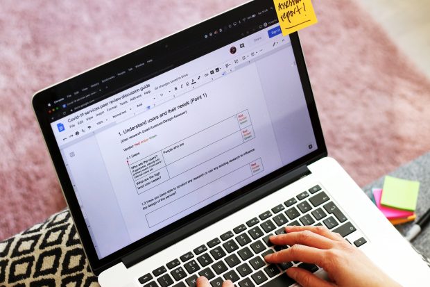 A person writing a COVID-19 services peer review discussion report on a laptop computer, on the screen a headline reads: 1. Understand users and their needs (Point 1)