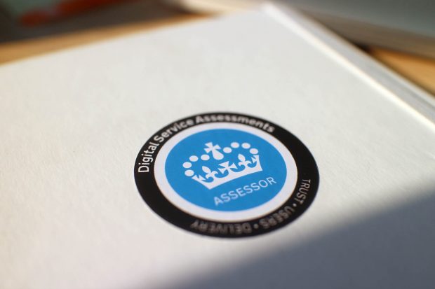 A sticker with the Crown symbol saying ‘ASSESSOR – Digital Service Assessments’ on a white notebook