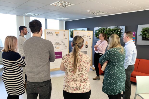 Members of the WMCA digital team standing in a circle discussing the GDS design principles that are pinned to a whiteboard they are looking at