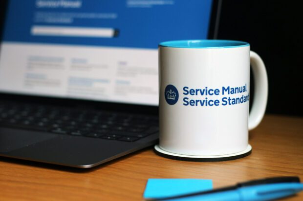 A cup saying Service Manual, Service Standard next to a computer showing the landing page of GOV.UK Service Manual